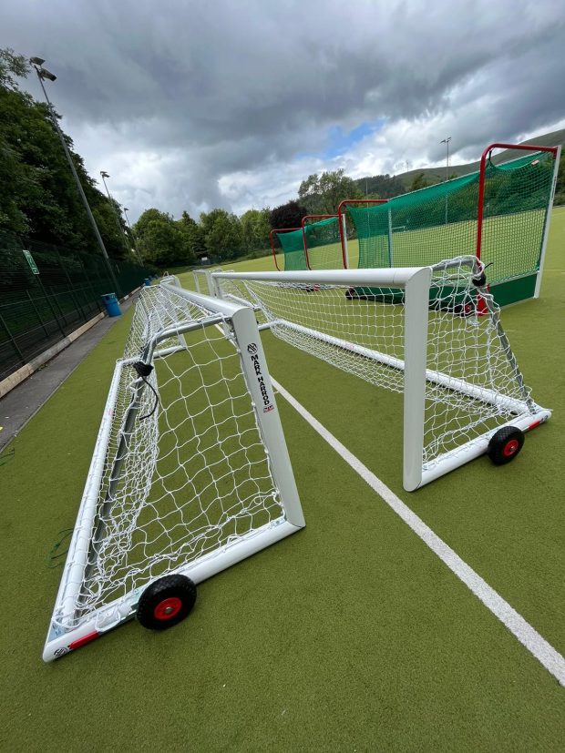 Full-sized football goal with wheels on an artificial pitch, positioned for play under a cloudy sky.