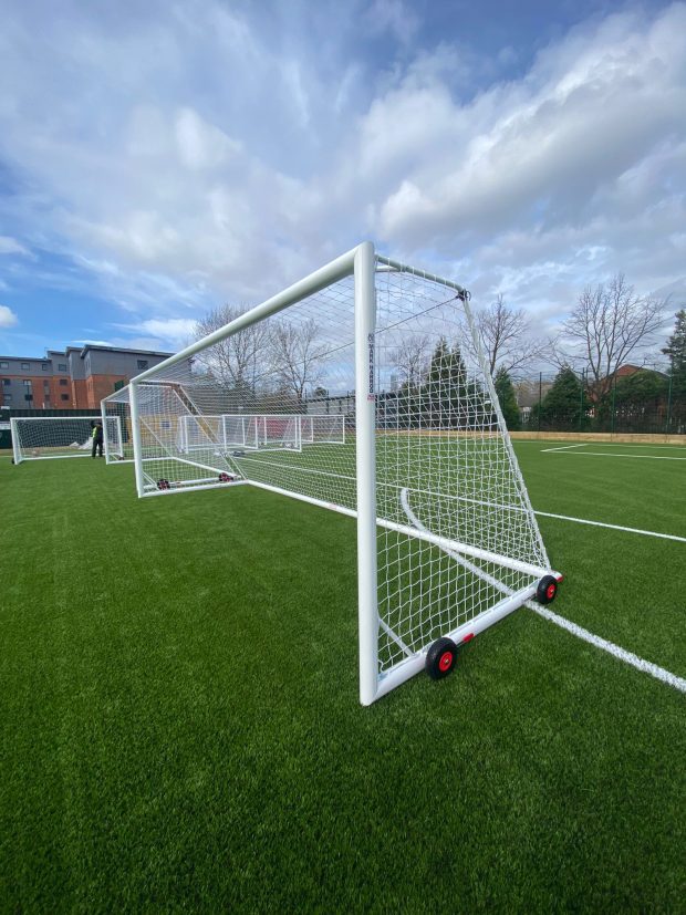 Two portable football goals with wheels on a synthetic pitch, positioned for training or match setup as part of proper goal post maintenance.